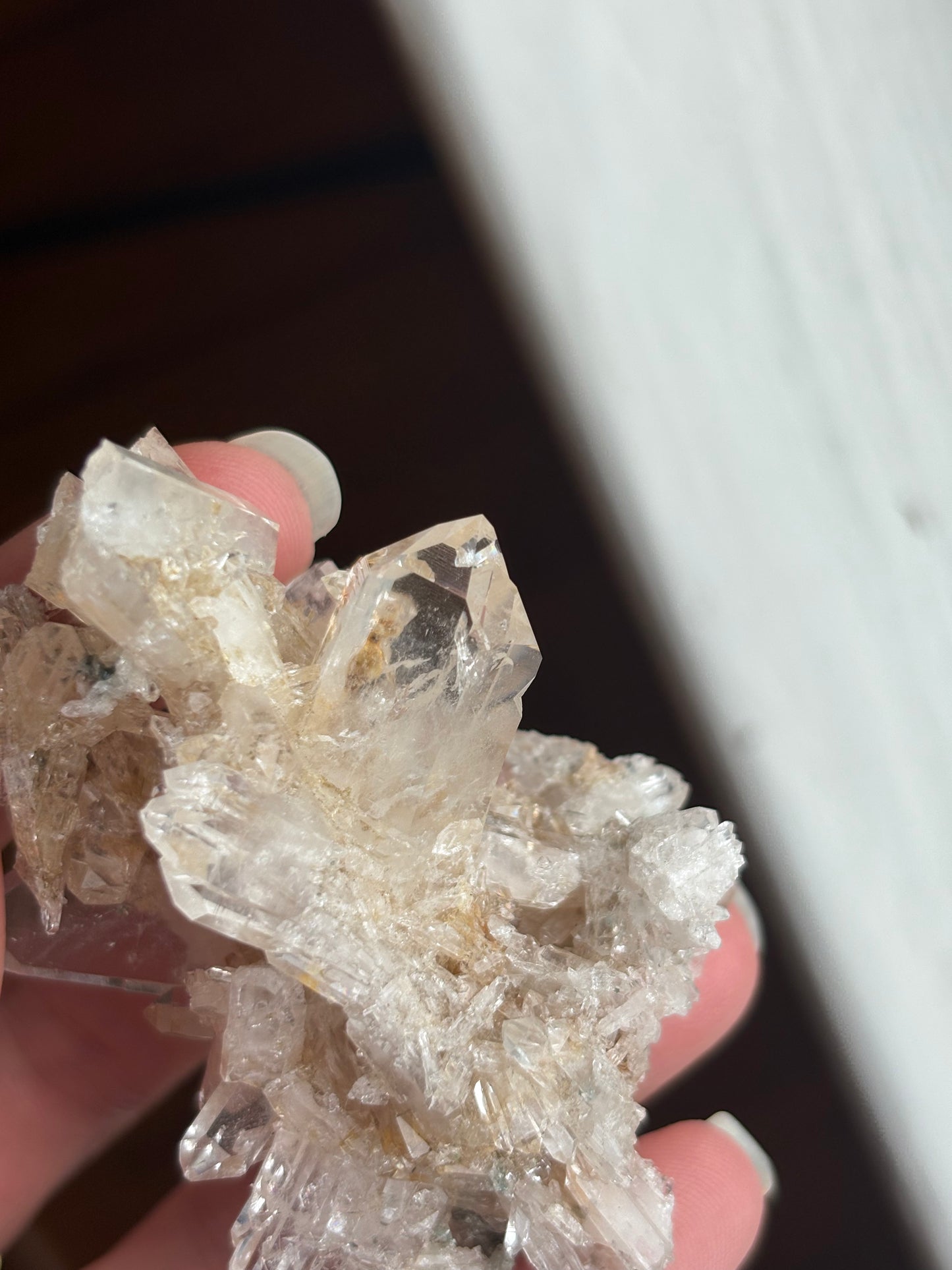 A close-up of a hand holding a clear quartz crystal cluster with natural inclusions, including a tiny reverse manifestation quartz inside 