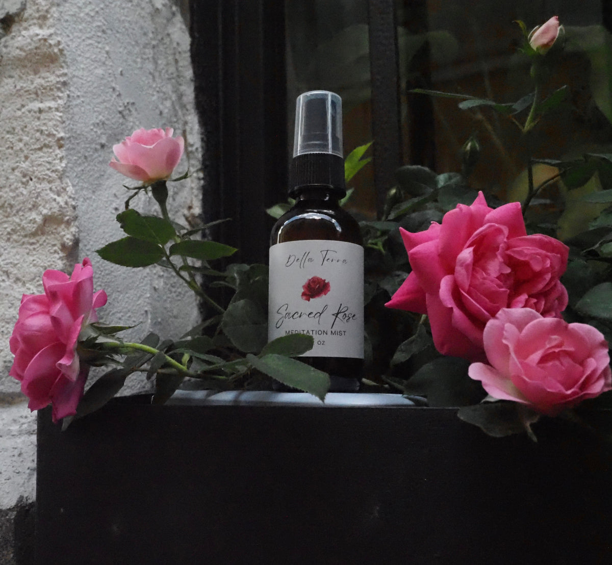 Sacred Rose Meditation Mist by Della Terra beside a window box of roses in Italy — aromatherapy spray for calm, grounding and meditation