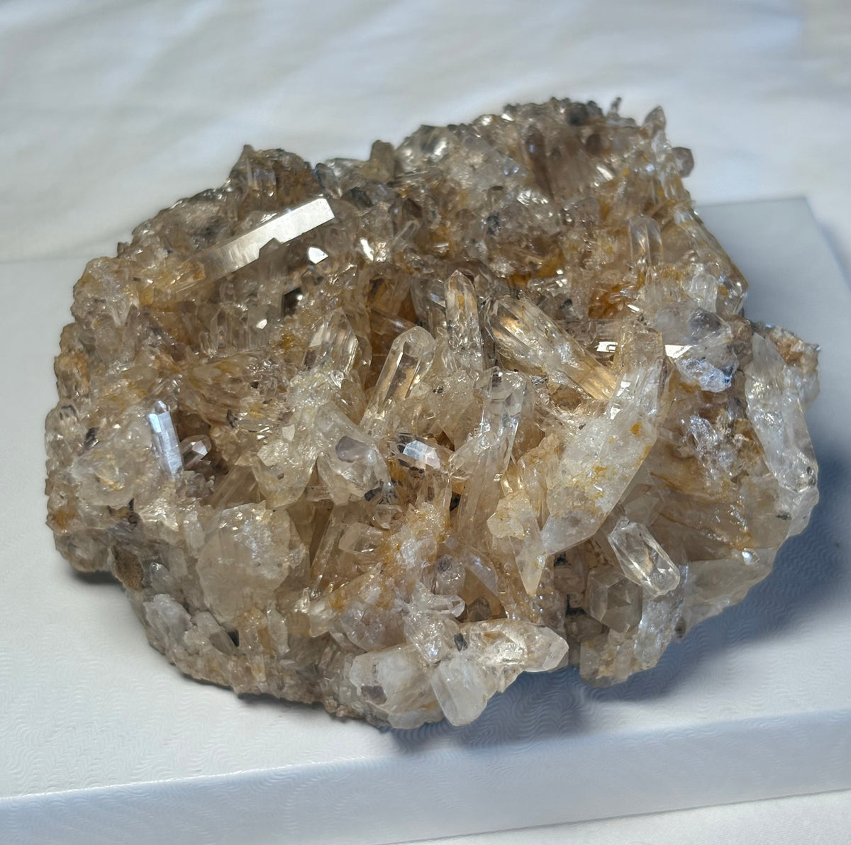 A cluster of golden healer colombian quartz crystals with a golden color, displayed on a white surface.